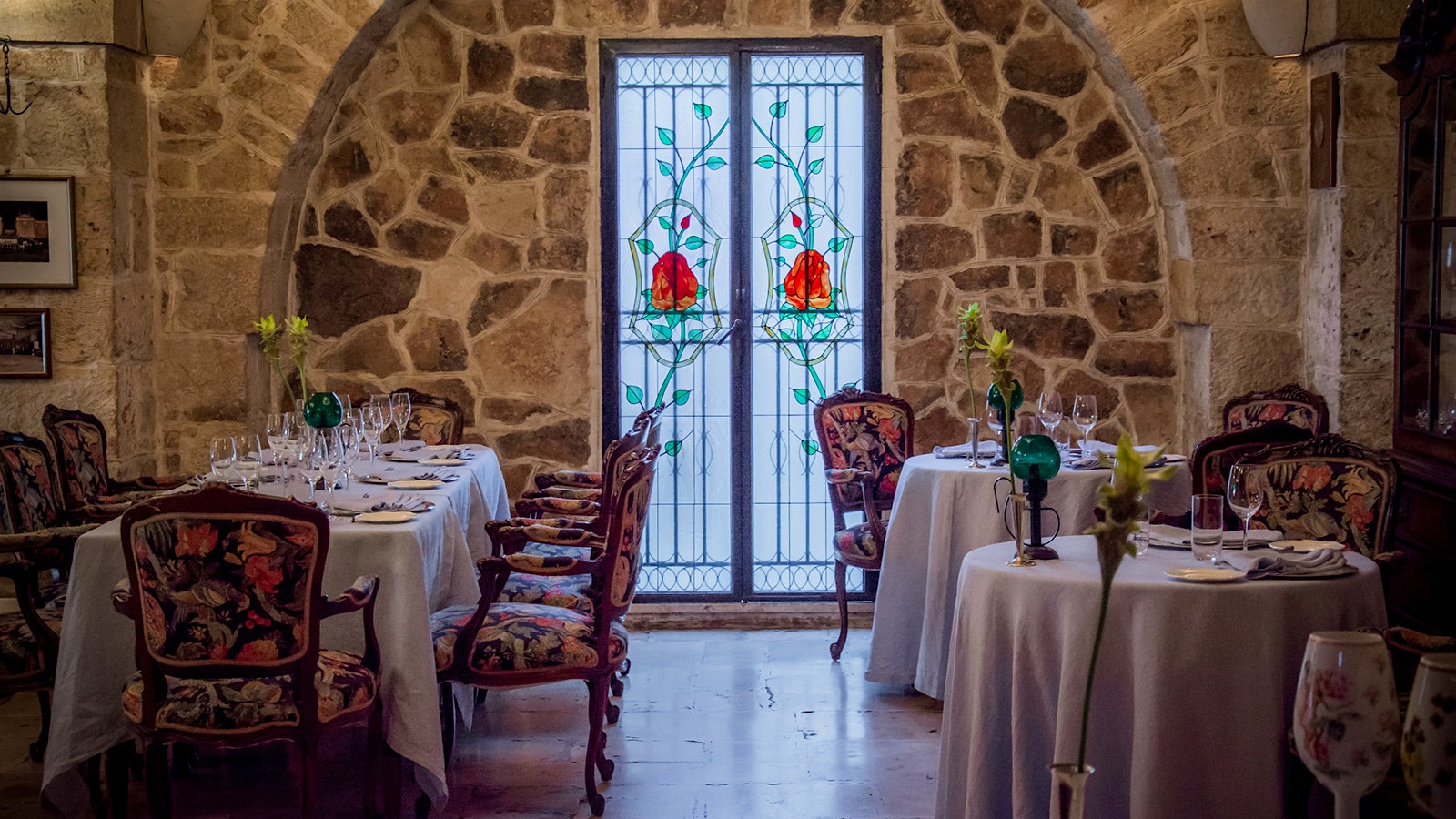 Tables set in the dining room of Il Poeta Contadino, with stone walls, floral-decorated chairs and a stained glass window depicting roses
